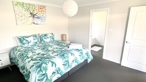 A bedroom with a bed, a nightstand, a wall-mounted lamp, and a door.