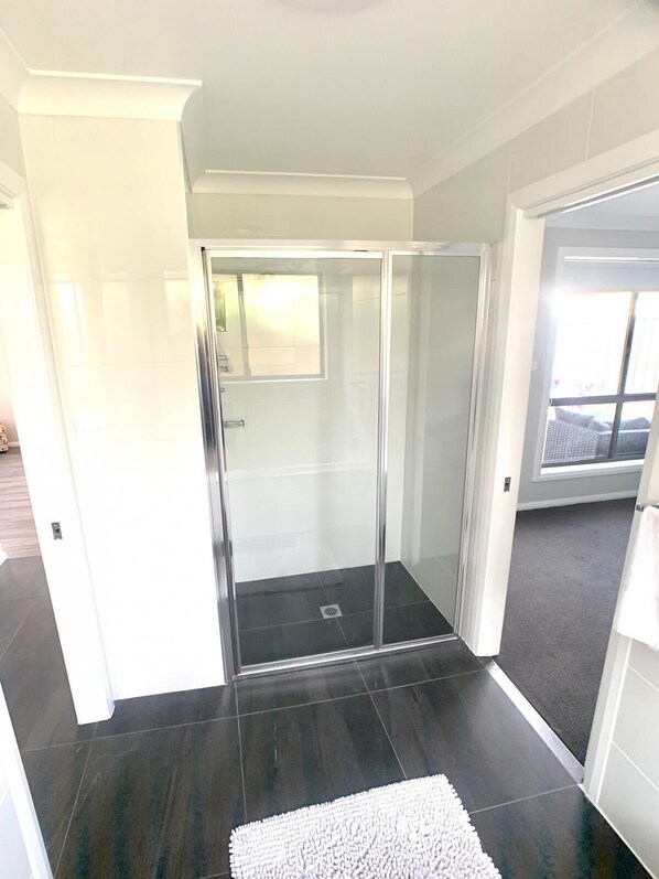 A modern bathroom with a glass shower enclosure, dark tiled flooring, and a white rug.