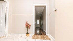 A hallway with a wooden floor, a potted plant, and a rug leading to a door. - Kinross on Cox • Cosy Retreat • Opposite KWS (Orange)