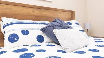 Un lit avec une couvre-lit à pois blancs et bleus, une tête de lit en bois et deux oreillers à pois bleus.