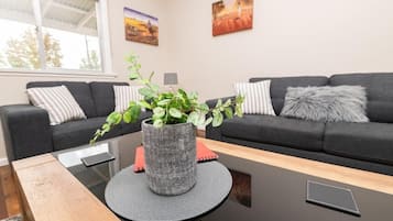 Un salon moderne avec un canapé gris foncé, une table basse ronde et un tapis gris, ainsi qu’une plante en pot.