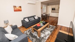 A modern living room with a sofa, coffee table, and artwork on the wall. - Kinross on Cox • Cosy Retreat • Opposite KWS (Orange)