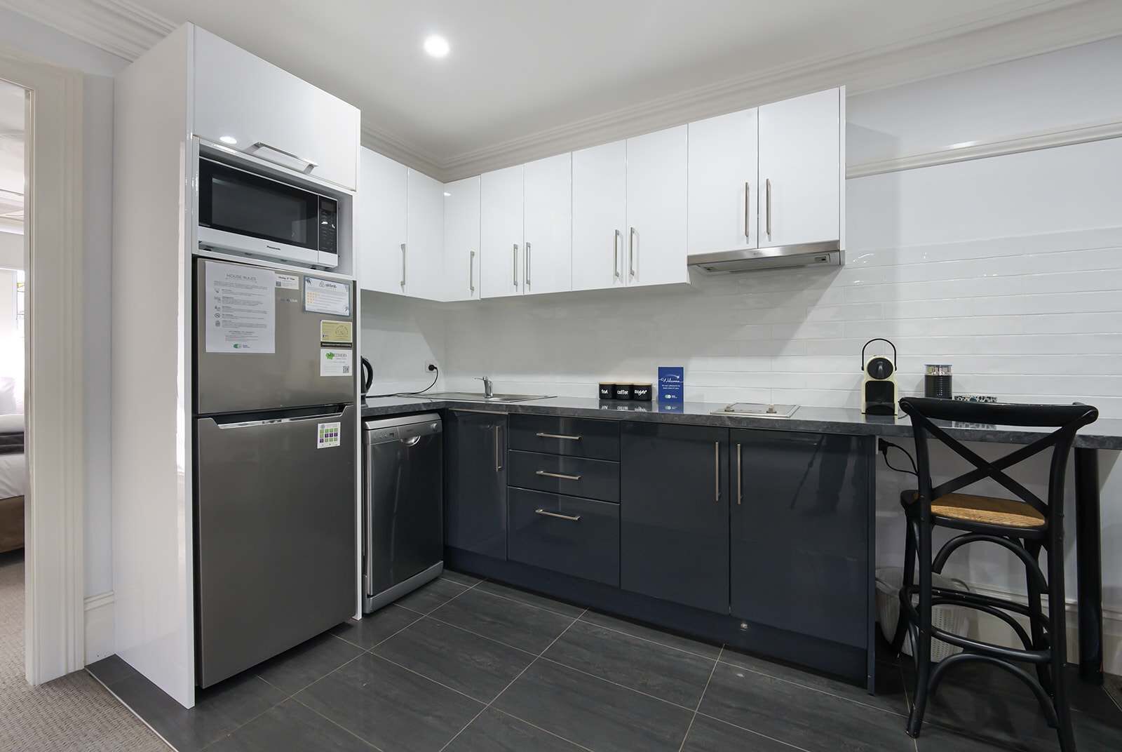 A modern kitchen with white cabinets, a stainless steel refrigerator, a microwave, and a coffee machine.