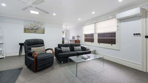 A modern living room with a sofa, armchair, and glass coffee table, white walls, and a ceiling fan.