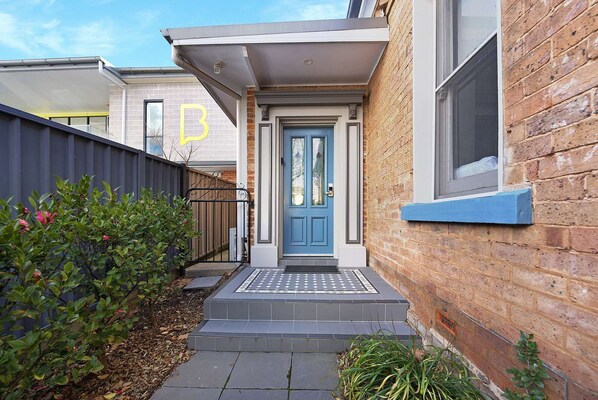 A residential building with a blue front door, a small porch, and a brick exterior. - Blue Door Apartment 2 | CBD, Ideal for Work (Orange)