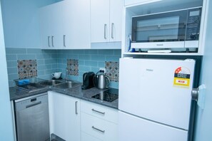 Una cucina compatta con mobili bianchi, un forno a microonde, un frigorifero, una lavastoviglie e un bollitore.