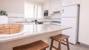 Cozinha com armários brancos, geladeira branca, micro-ondas, fogão e uma ilha grande com cesta e banquetas.