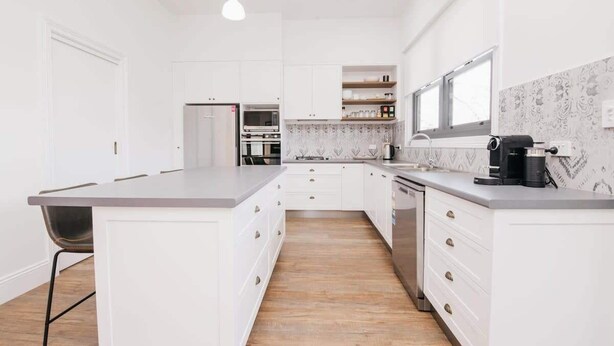 Een moderne keuken met witte kasten, een centraal eiland, een inbouwoven en een koffieapparaat.