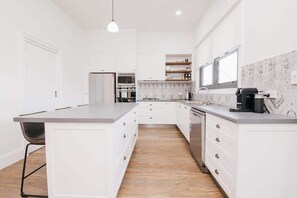 A modern kitchen with white cabinetry, a central island, a built-in oven, and a coffee machine.