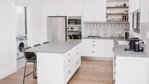 Een moderne keuken met witte kasten, een centraal eiland, een inbouwoven en een koffieapparaat.