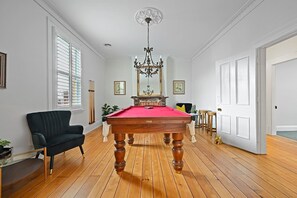 Quarto com mesa de bilhar, uma poltrona preta, um candelabro e piso de madeira.