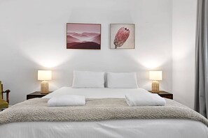 Cama com lençóis brancos, duas almofadas, um cobertor fofo e duas luminárias de cabeceira.