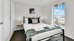 A bedroom with a bed, a nightstand, a lamp, a window with a view, and a ceiling light. - Emmaville - Modern, Convenient & Pets Allowed (Orange)