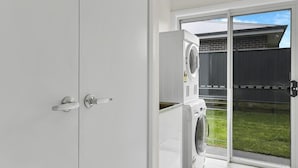 A laundry room with a washing machine and dryer, a sliding glass door to a backyard, and a white cabinet. - Emmaville - Modern, Convenient & Pets Allowed (Orange)