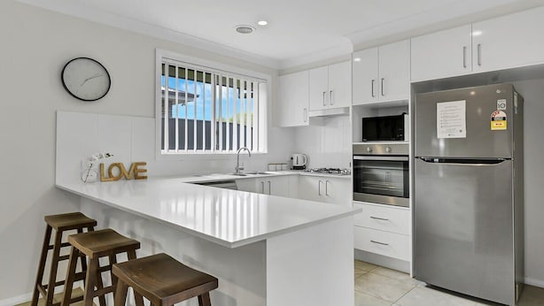 A modern kitchen with white cabinetry, a stainless steel refrigerator, a gas stove, and a large island with stools. - Emmaville - Modern, Convenient & Pets Allowed (Orange)