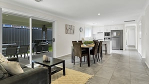 A modern kitchen with white cabinets, a refrigerator, and a dining area with a table and chairs. - Emmaville - Modern, Convenient & Pets Allowed (Orange)
