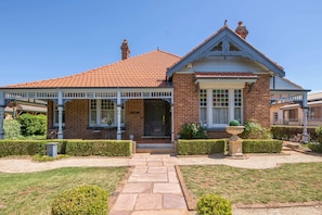 A two-story house with a red-tiled roof, a front porch with white railings, and a brick facade.