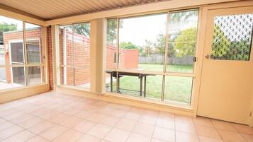 A spacious room with large windows, a tiled floor, and a door with a mesh screen.
