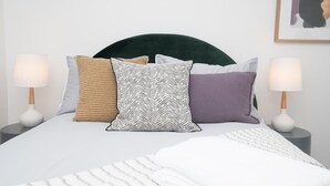 Ein Bett mit dunklem Kopfteil, mehreren Kissen und zwei Nachttischlampen.