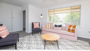 Ein Wohnzimmer mit einer Couch, einem Sessel und einem runden Couchtisch, einem Deckenventilator und einem Fenster mit Jalousien.