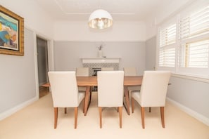 A dining room with a wooden table and four chairs, a white pendant light, and a fireplace with a tiled surround.