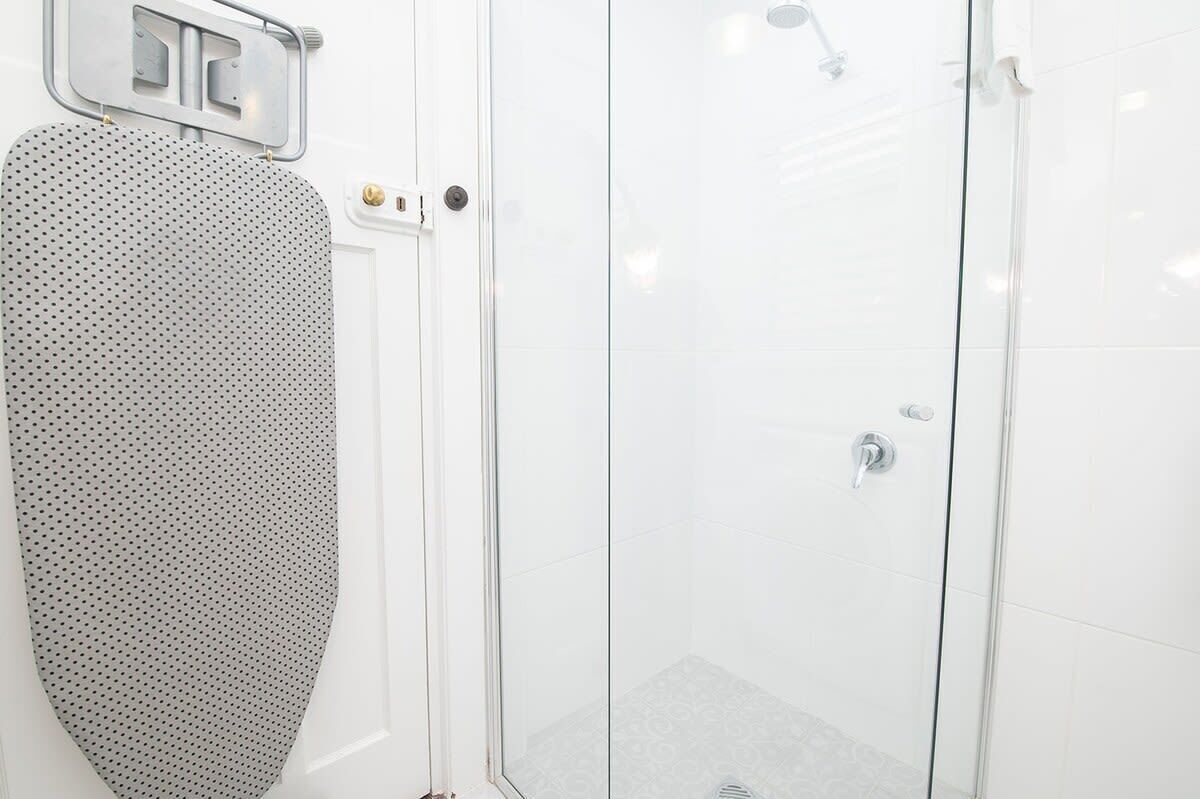 A modern bathroom with a glass shower enclosure, a white tiled wall, and a shower control panel.