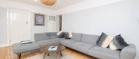 Un salon moderne avec un canapé d’angle gris, une table basse ronde et un luminaire suspendu.
