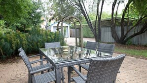 Una mesa con cubierta de vidrio y sillas de mimbre en un jardín.