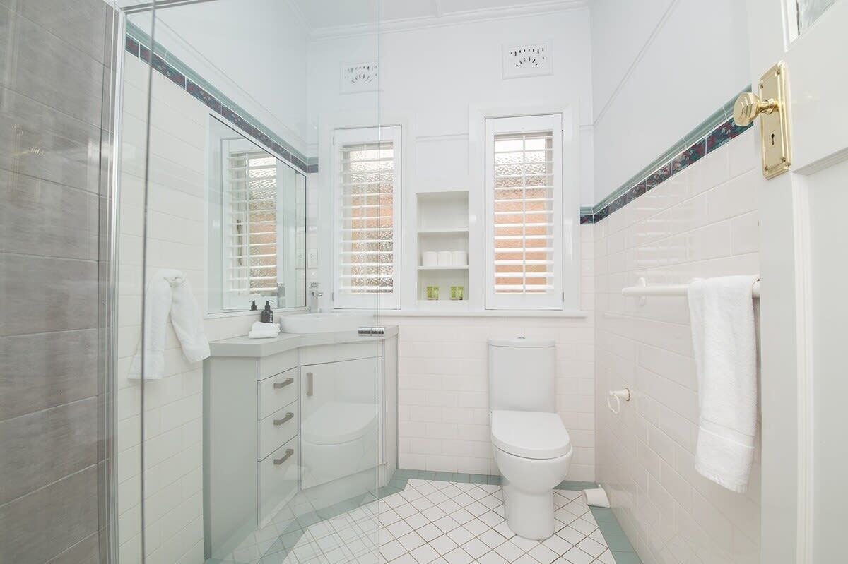 A modern bathroom with a glass shower enclosure, white tiles, and a toilet.