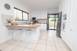 Una cocina moderna con armarios blancos, una isla de madera con taburetes altos y electrodomésticos de acero inoxidable, incluyendo un microondas.