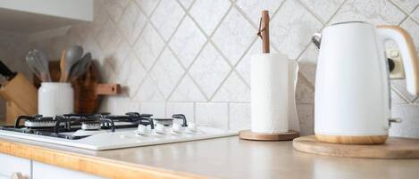 A kitchen with a gas stove, a roll of paper towels, and a kettle on the counter.