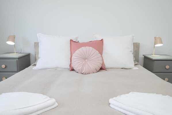 Una cama con dos mesitas de noche, cada una con una lámpara, y un arreglo de almohadas.