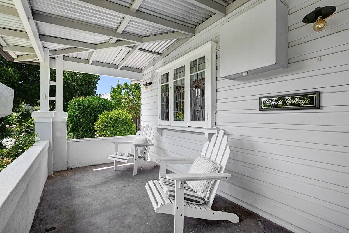 Eine überdachte Veranda mit weißen Adirondack-Stühlen und einem Schild mit der Aufschrift 'Bindi Cottage'.