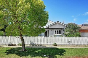 A residential house with a white picket fence, a tree in the foreground, and a clear blue sky.