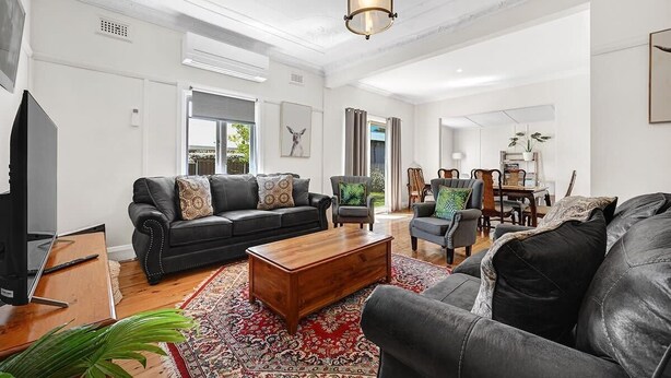 A living room with a black leather sofa, a wooden coffee table, and a patterned rug. - Bindi Cottage | Classic Charm, Short Stroll to CBD (Orange)