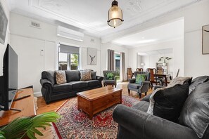 A living room with a black leather sofa, a wooden coffee table, and a patterned rug. - Bindi Cottage | Classic Charm, Short Stroll to CBD (Orange)