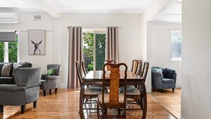 A dining area with a wooden table and chairs, a sofa, and a blue armchair. - Bindi Cottage | Classic Charm, Short Stroll to CBD (Orange)