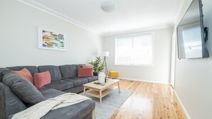 A modern living room with a grey sofa, a wooden coffee table, and a large window with blinds. - Sweet Caroline. Sunroom & Garden. Orange. (Orange)