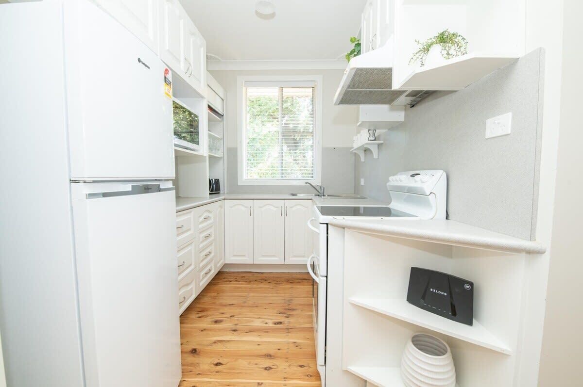 A kitchen with white cabinets, a wooden floor, a window with blinds, and a built-in oven.