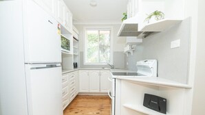 A kitchen with white cabinets, a wooden floor, a window with blinds, and a built-in oven. - Sweet Caroline. Sunroom & Garden. Orange. (Orange)
