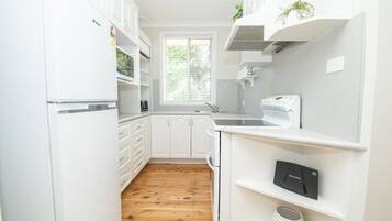 A kitchen with white cabinets, a wooden floor, a window with blinds, and a built-in oven.