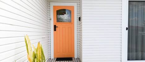 A house with a white exterior, an orange door, and a patterned tile floor.