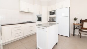 Una cocina con gabinetes blancos, microondas, estufa y refrigerador.
