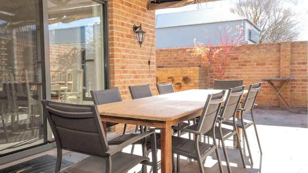 Un patio al aire libre con una mesa y sillas de madera, un muro de ladrillo y una puerta de cristal.