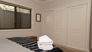 Un dormitorio con cama, ventana, mesita de noche y varios armarios blancos.