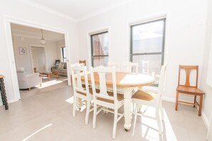 A dining area with a round table and white chairs, large windows, and a view of the outside.