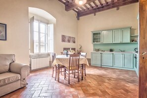 A dining area with a table and chairs, a sofa, a window, and a kitchen with cabinets.