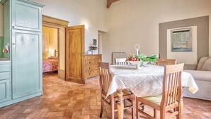 Un comedor con una mesa para dos personas, sillas de madera, un armario y una puerta que da a otra habitación.