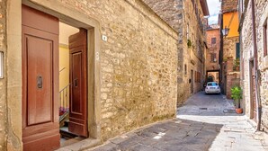 Una estrecha calle de piedra con la entrada de un edificio, una puerta a la vista y un coche estacionado al fondo.