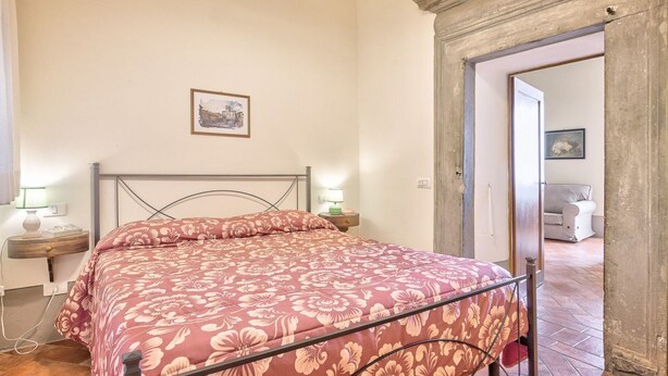 Un dormitorio con una cama, lámparas de noche, un cuadro en la pared y una puerta que da a otra habitación.